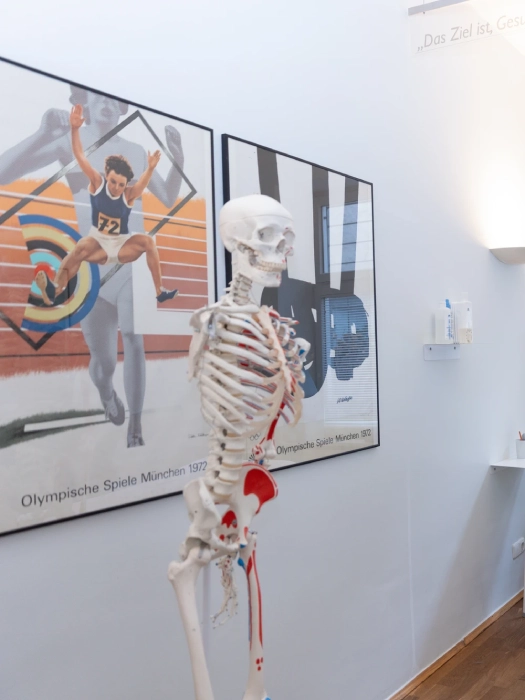 Skelett mit rot markiertem Herz-Kreislauf-System vor Plakat Olympische Spiele München 1972 mit Sportler und Zielscheibe